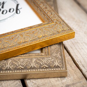 May include: Two ornate picture frames, one gold and one silver, with intricate designs. The gold frame is on top of the silver frame.