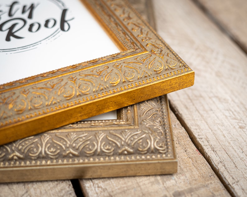 May include: Two ornate picture frames, one gold and one silver, with intricate designs. The gold frame is on top of the silver frame.