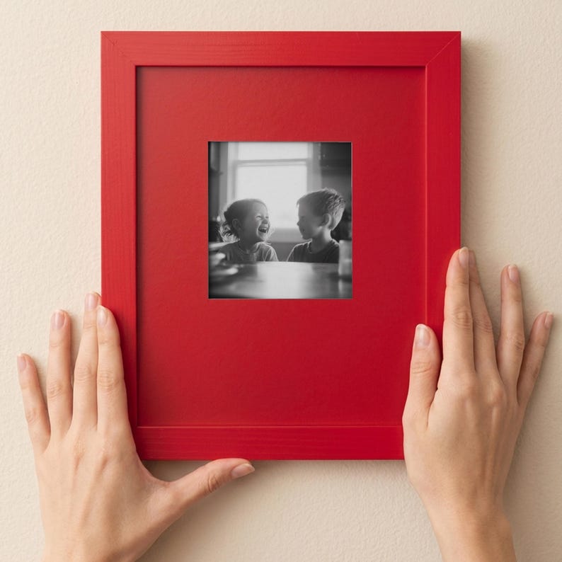 A person's hands are holding a red picture frame with a black and white photograph of two children inside it.