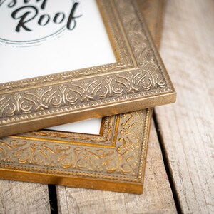 May include: Two ornate gold picture frames with intricate designs. The top frame has the text "Rustic Roof" printed on the white mat.