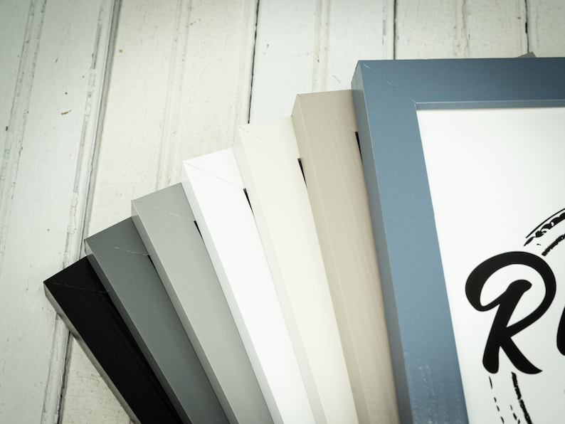 May include: A collection of picture frames in various colors, including black, gray, white, and blue. The frames are arranged in a fan shape, showcasing their different hues and styles. The frames are made of wood and have a clean, modern design.