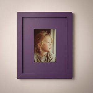 A young girl with blonde hair is the focus of the image, captured in a thoughtful gaze within a purple framed picture.