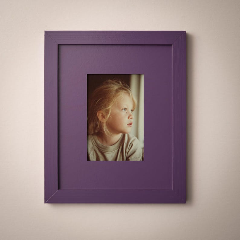 A young girl with blonde hair is the focus of the image, captured in a thoughtful gaze within a purple framed picture.