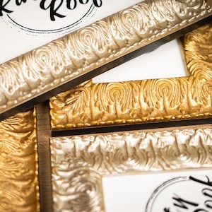 May include: Three ornate picture frames with gold and silver finishes. The frames have a decorative, textured design. The top frame has the word "Book" written in black ink.