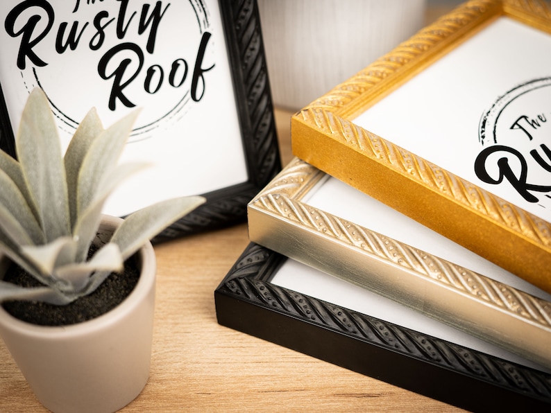 May include: Three picture frames with rope-like detailing around the edges. The frames are stacked on top of each other, with the black frame on the bottom, the silver frame in the middle, and the gold frame on top. The top frame has the text "The Rusty Roof" printed on the inside.