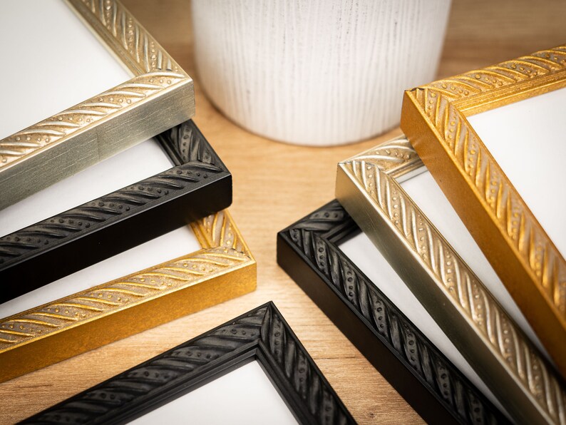 May include: Five picture frames in different colors, including black, gold, and silver. The frames have a decorative, rope-like design around the edges.