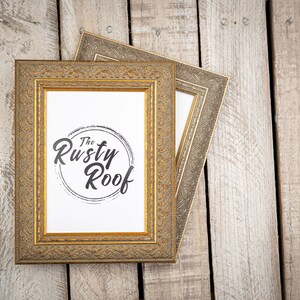 May include: Two gold picture frames with ornate detailing, the top frame is slightly offset from the bottom frame. The bottom frame has a white mat and a black and white logo that says "The Rusty Roof".