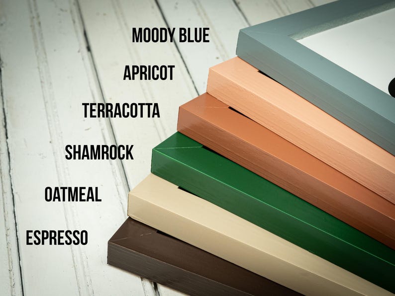 May include: A stack of picture frames in various colors, including Moody Blue, Apricot, Terracotta, Shamrock, Oatmeal, and Espresso. The frames are angled, showcasing their different hues and the text labels for each color.