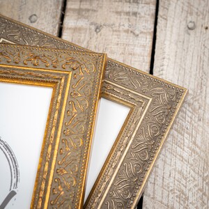 May include: Two ornate gold picture frames with a white mat and a white background. The frames have a decorative, embossed design.