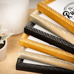 May include: A stack of four picture frames with ornate rope-like detailing. The frames are in black, silver, gold, and gold with a darker finish. The top frame has a white label with the text "The Rusty Pig".