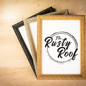 May include: Three picture frames stacked on top of each other. The top frame is gold with a rope-like design. The middle frame is silver with a rope-like design. The bottom frame is black with a rope-like design. The top frame has a white background with the text "The Rusty Roof" in black.