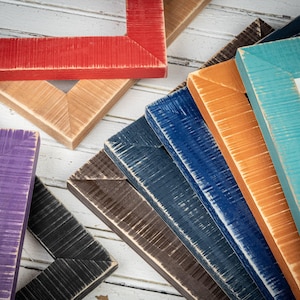 May include: A collection of colorful wooden picture frames in various shades, including red, teal, orange, blue, brown, black, and purple. The frames have a distressed, rustic finish, and are arranged on a white wooden surface.