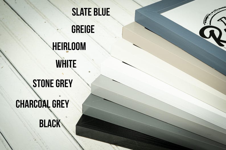 May include: A stack of painted wooden picture frames in various colors, including slate blue, greige, heirloom, white, stone grey, charcoal grey, and black. The frames are angled, showcasing the different color options.