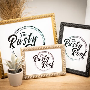 May include: Three gold and black picture frames with the text "The Rusty Roof" in a circle with a watercolor-like design. The frames are on a wooden surface.
