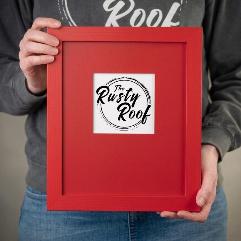 A person is holding a red picture frame with the text "The Rusty Roof" on it.