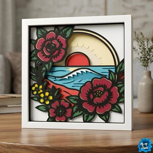 May include: A framed, layered paper art piece featuring a sunset over the ocean, with red roses and yellow flowers. The artwork is set in a white frame and sits on a wooden table. The image has a nautical theme.