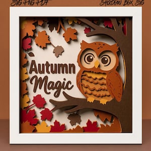 May include: A layered paper shadow box in a white frame featuring a brown owl perched on a tree branch. The design includes red, orange, and yellow maple leaves and the text Autumn Magic. The top corners display the text SVG PNG PDF and SHADOW BOX SVG.