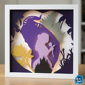 May include: A framed paper cut artwork depicting a woman with a rose, a castle, and a beast silhouette. The layered design uses purple, yellow, and green against a white backdrop, all encased in a white frame, creating a 3D effect.