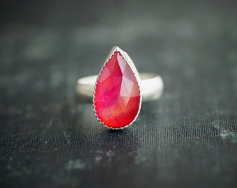 May include: A silver ring with a teardrop-shaped red gemstone.