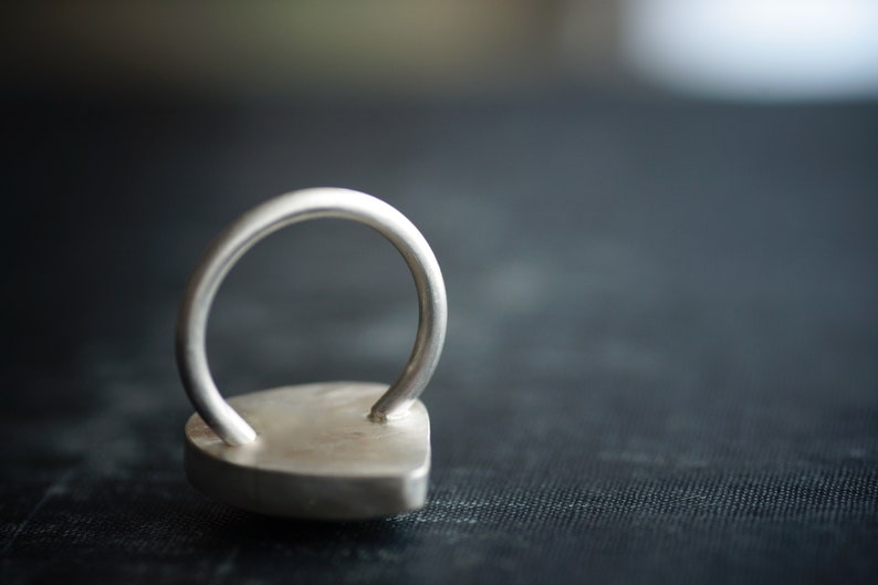 May include: A silver ring with a heart-shaped design. The ring is made of metal and has a smooth, polished finish.