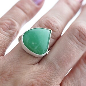 May include: A teardrop-shaped green gemstone ring set in a silver band.