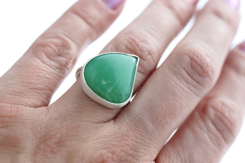 May include: A teardrop-shaped green gemstone ring set in a silver band.