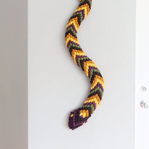 May include: A crocheted snake wall hanging with a purple, yellow, and green chevron pattern.