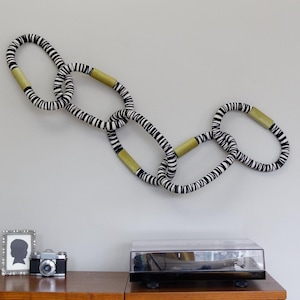 May include: A black and white striped chain with gold accents hangs on a wall above a wooden record player cabinet. The cabinet has a record player on top and shelves below filled with vinyl records.