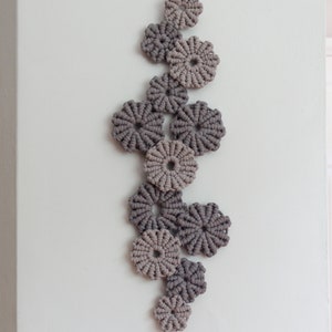 May include: A wall hanging made of macrame with a series of circular shapes in shades of gray and beige.