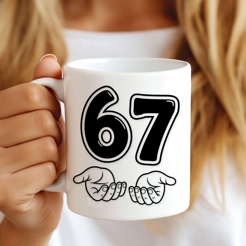Pu&ograve; includere: Tazza in ceramica bianca con il numero 67 in grassetto nero e contorno bianco. Sotto i numeri ci sono due mani stilizzate. La tazza &egrave; tenuta da una persona.