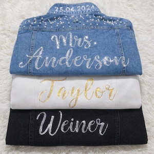 May include: Three denim jackets, each with personalized text. The top jacket is light blue with the text "Mrs. Anderson" in rhinestones and pearls. The middle jacket is white with "Taylor" in gold rhinestones. The bottom jacket is black with "Weiner" in rhinestones.