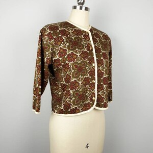May include: A brown and cream cardigan with a floral pattern. The cardigan has a white trim and buttons down the front.