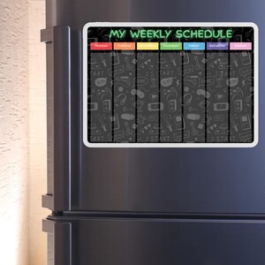 May include: A white magnetic dry-erase weekly schedule board with a black background and colorful headings for each day of the week. The board is decorated with a variety of video game-themed doodles, including controllers, swords, and hearts.