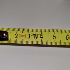 May include: A yellow Stanley measuring tape with black markings. The tape shows measurements in inches and feet. The numbers 2, 3, 4, 5, and 6 are visible. The Stanley logo is also visible.