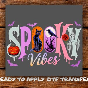May include: A DTF transfer sheet featuring the text SPOOKY VIBES in a dripping font. The design includes a jack-o'-lantern, a black cat, a raven on a tree, a ghost holding a red flower, and purple bats against a dark gray background.