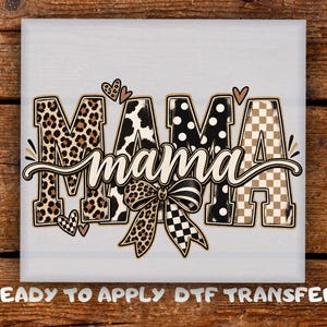 May include: A DTF transfer design featuring the word MAMA in large block letters with varied patterns including leopard print, cow print, black polka dots, and a tan checkerboard. The word mama is written in cursive script across the center with a bow.