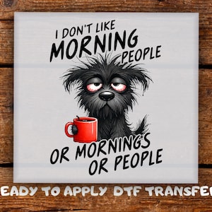 May include: A square, light grey graphic featuring a cartoon dog with tired eyes holding a red mug. The text reads "I DON'T LIKE MORNING PEOPLE OR MORNINGS OR PEOPLE" in black. Below the text is "READY TO APPLY DTF TRANSFER".