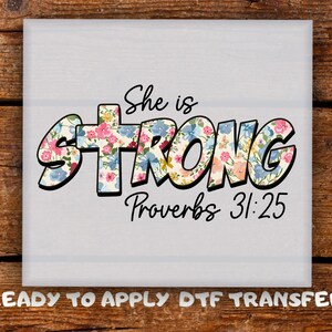 May include: A square, light gray image with the words "She is STRONG" in a floral design, with the text "Proverbs 31:25" below. The phrase "READY TO APPLY DTF TRANSFER" is at the bottom.