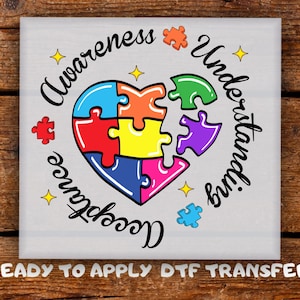 May include: A square image featuring a heart-shaped puzzle design in multiple colors, surrounded by the words "Awareness, Understanding, Acceptance." Additional puzzle pieces and stars are scattered around the heart. The text "READY TO APPLY DTF TRANSFER" is at the bottom.
