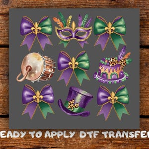 Puede incluir: Una colección de gráficos con temática de Mardi Gras sobre un fondo gris. El diseño incluye lazos morados y verdes, una máscara, un tambor, un pastel y un sombrero de copa. El texto "READY TO APPLY DTF TRANSFER" está en la parte inferior.