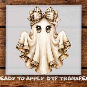 May include: A graphic illustration of a ghost wearing a large leopard print bow on its head. The ghost has large brown eyes with long eyelashes and a beige sheet body with leopard print trim at the bottom edges. Text reads: READY TO APPLY DTF TRANSFER.