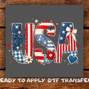 May include: A patriotic design featuring the word "USA" in red, white, and blue. The letters are decorated with stars, bows, and floral accents, with a patchwork effect. The text "READY TO APPLY DTF TRANSFER" is at the bottom.