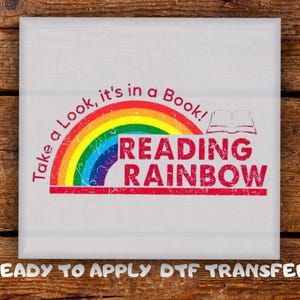 May include: A white square with a colorful rainbow design and the words "Take a Look, it's in a Book!" and "READING RAINBOW" in red. The phrase "READY TO APPLY DTF TRANSFER" is at the bottom.