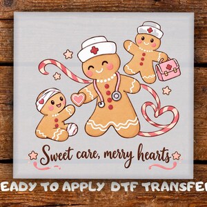 May include: A DTF transfer featuring three gingerbread characters: one wearing a nurse hat and stethoscope, one with a bandage on its head, and one holding a medical bag. A candy cane swirls around them. The text reads Sweet care, merry hearts.