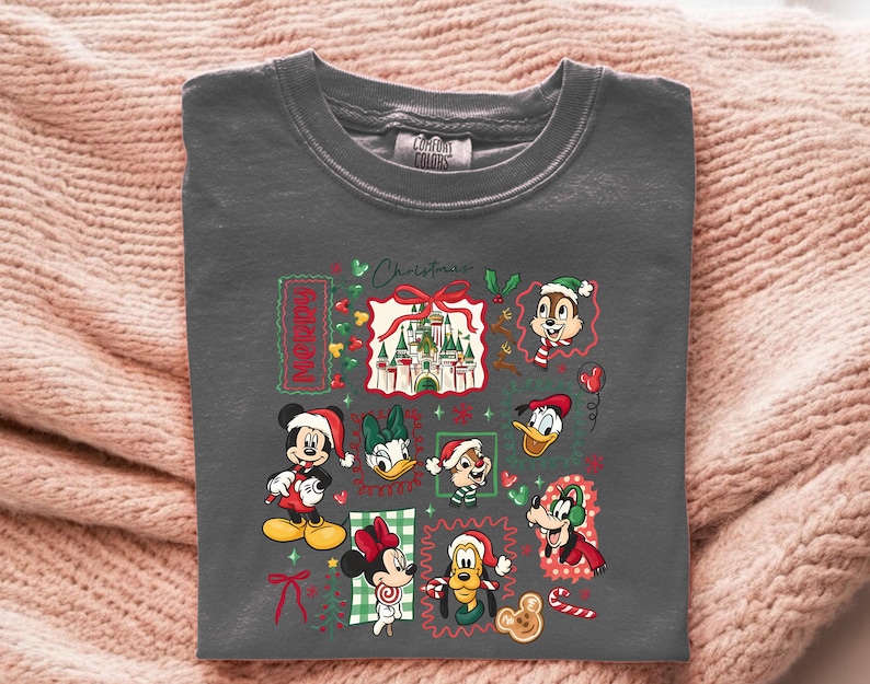 May include: Dark gray crew neck t-shirt featuring a colorful Christmas design. The design includes Mickey Mouse, Minnie Mouse, Donald Duck, and other Disney characters in festive attire. The word "Christmas" is also visible.