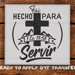 May include: A square, off-white DTF transfer with black text and graphics. The design includes a cross, mountains, and the words "Fui Hecho Para Servir" and "1 Co. 15:58". The phrase "Ready to Apply DTF Transfer" is at the bottom.