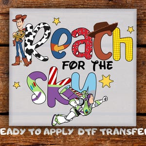 May include: A gray square featuring the phrase "Reach for the Sky" in colorful, stylized letters. The design includes cartoon characters Woody and Buzz Lightyear, with star accents. The text "READY TO APPLY DTF TRANSFER" is at the bottom.