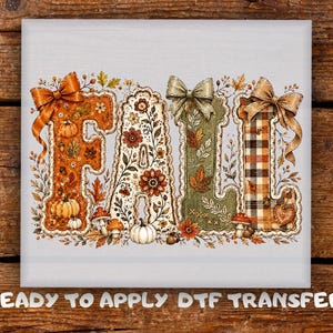 May include: A ready to apply DTF transfer featuring the word FALL in large decorative letters. The letters are adorned with autumn motifs including pumpkins, mushrooms, leaves, and flowers, accented with orange, green, and plaid bows.