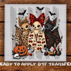 May include: A DTF transfer featuring three cartoon bats with large eyes. The left bat has a leopard print wing, the centre bat wears a red skull-patterned bow, and the right bat has black wings with red skulls. Includes a pumpkin, skulls, and potions.