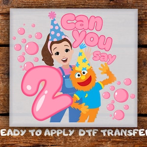 Peut inclure: Transfert DTF avec une illustration de dessin animé. Il présente le texte "Can You Say" et le chiffre "2". L'image comprend deux personnages de dessins animés, des bulles roses et des chapeaux de fête. Les mots "READY TO APPLY DTF TRANSFER" sont en bas.